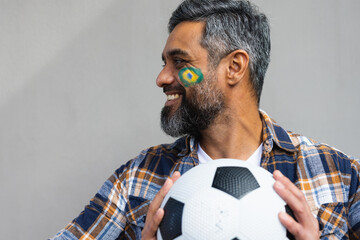 Happy biracial man with football and flag of brazil on his cheek - Powered by Adobe