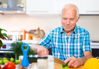 senor man preparing fresh vegetable salad at home in the kitchen
