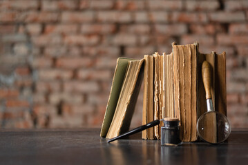 Stack of books, inkpot, quill pen and magnifying glass on the vintage table background. Back to school. Education concept background.