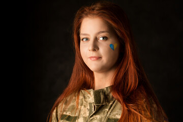 A young woman in camouflage with a blue and yellow heart on her face.