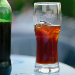 Selective focus shot of a glass of black Radler beer with ice next to the bottle on a table in a cafe terrace