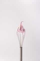 Whisk with cream on a white background. Pink whipped cream made from protein and sugar on a whisk....