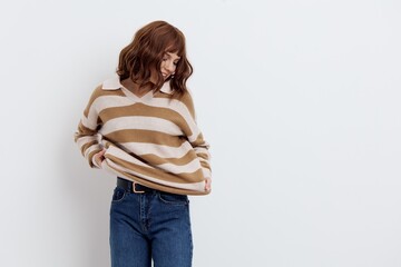 a beautiful, woman stands in a stylish striped sweater and pulling it from below looks at the sweater and smiles pleasantly. Horizontal photo with an empty space for inserting an advertising layout