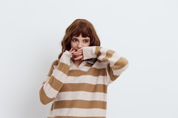 a sweet, pleasant woman with a short haircut stands on a light background in a stylish beige sweater and looks at the camera holding her hand near her face