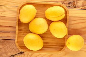 Several bright yellow juicy pineapple apricots with a wooden tray on a wooden table, macro, top view.