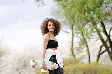 Young african american  woman riding on the skateboard on the road in the park