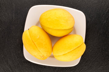 Three bright yellow juicy pineapple apricots with a white saucer on a slate stone, macro, top view.