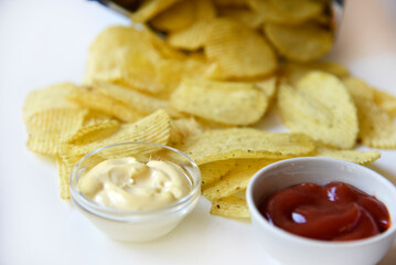 Yellow fluted chips from a bag with sauce on a white background. Delicious fast food fried potatoes.