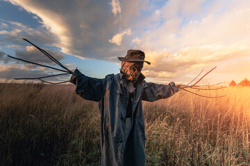 Scary scarecrow in a hat and coat on a evening autumn field during sunset. Spooky Halloween holiday...