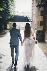 Rain drops on background of stylish bride and groom walking under umbrella and holding hands at old...