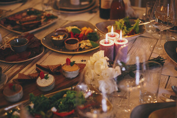 Stylish delicious table with food and drinks, burning candles and flowers at evening provence wedding reception in restaurant. Christmas feast or new year party. Luxury catering at banquets