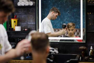 Young male barber arranging haircut of the teenage boy in barbershop