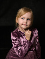 emotional little red-haired blonde girl in a lilac dress on a black background