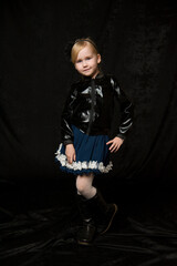 funny little blonde girl in a leather jacket and a blue skirt  on black background