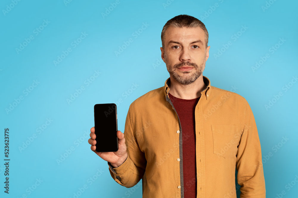 Poster Serious Man Showing Smartphone With Empty Screen On Blue Background