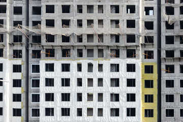 The facade of a new monolithic apartment building under construction in the process of insulation with a safety net against the fall of builders.