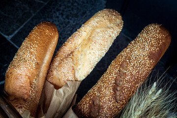 3 fresh wheat loaves with sesame seeds on a dark background.
