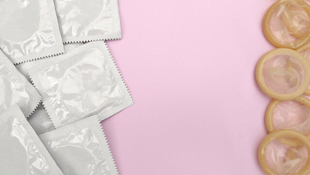 Many white packages of unopened condoms on a pink background.