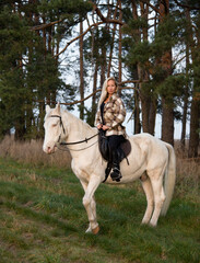 young beautiful blond smiling woman with long hair  riding a white horse with blue eyes in autumn field	