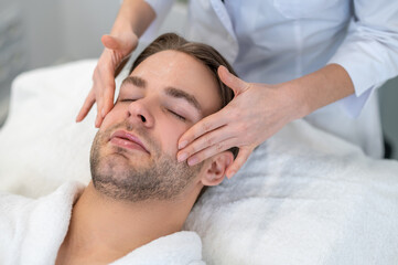Fototapeta na wymiar Female professional doing face massage to a male client