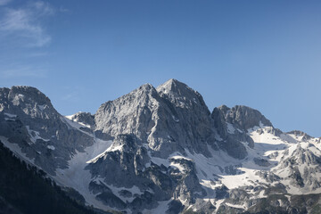 Fototapeta na wymiar stunning high grey mountain with snow fields on a sunny day and blue sky, alpine area 