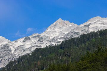 Fototapeta na wymiar stunning high grey mountain with snow fields on a sunny day and blue sky, alpine area