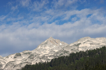 stunning high grey mountain with snow fields on a sunny day and blue sky, alpine area