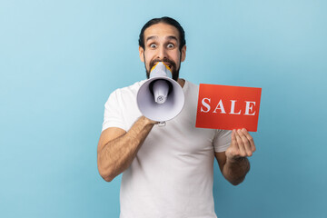 Portrait of excited man with beard wearing white T-shirt holding card with sale inscription and...
