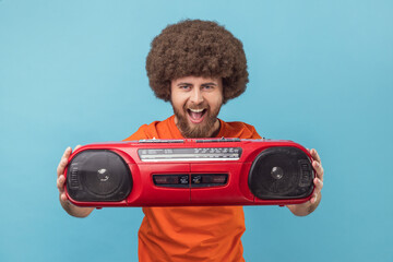 Portrait of excited happy man with Afro hairstyle wearing orange T-shirt holding out red tape...