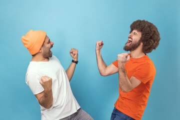 Portrait of two young adult hipster men showing yes gesture and screaming celebrating victory,...