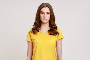 Portrait of pretty serious bossy brown haired woman of young age in yellow casual T-shirt, looking at camera with suspicion and accusing. Indoor studio shot isolated on gray background.