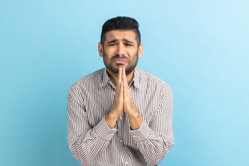 Portrait of businessman keeps palms pressed together, pleading angel, has innocent expressions,...