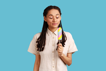 Optimistic woman with black dreadlocks holding sweet colorful ice cream wants to try delicious...