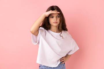 Portrait of little girl wearing white T-shirt peering into distance, looking far away with attentive view, searching on horizon and curious to discover. Indoor studio shot isolated on pink background.
