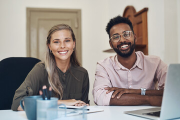Happy diverse employees working together on a project sitting in an office table satisfied with the partnership. Portrait of young colleagues with a positive mindset smiling about business growth