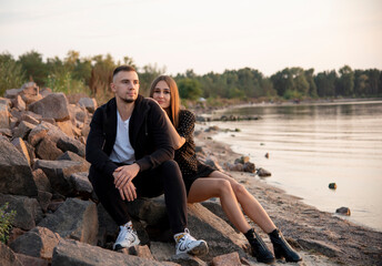 young beautiful couple sitting on the beach near river on sunset