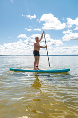 A man in shorts on a SUP board with an oar floats standing on the water against the blue sky.