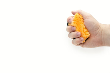 Orange sponge for washing dishes in a hand on a white background. A man's hand squeezes a sponge for washing or cleaning. Free space for text. The concept of cleanliness and housekeeping
