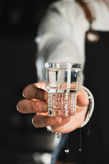 Vodka shot. Glass shot of alcohol. The bartender holds a glass shot with liquid. The trend drinks concept. Vertical photo
