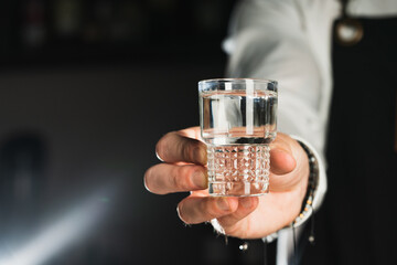 Vodka shot. Glass shot of alcohol. The bartender holds a glass shot with liquid. The trend drinks concept.