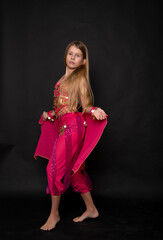 Obraz premium a young beautiful blonde girl in a pink outfit dances an oriental belly dance on black background