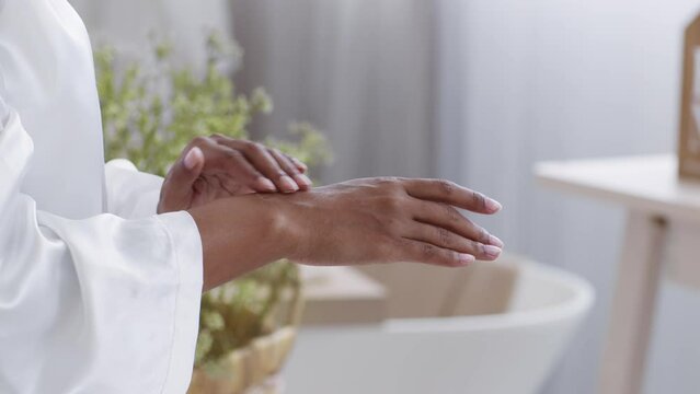 Skin treatment. Unrecognizable black woman rubbing dot of pampering skin on her hand, moisturizing body after bath