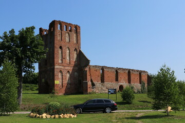 Ruiny kościoła gotyckiego z czerwonej cegły i stojący przed nim czarny samochód - obrazy, fototapety, plakaty