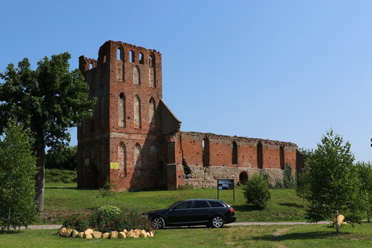 Fototapeta Ruiny kościoła gotyckiego z czerwonej cegły i stojący przed nim czarny samochód