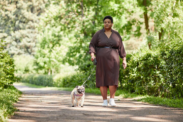 Full length portrait of elegant mature woman wearing dress while walking little dog in park, copy...