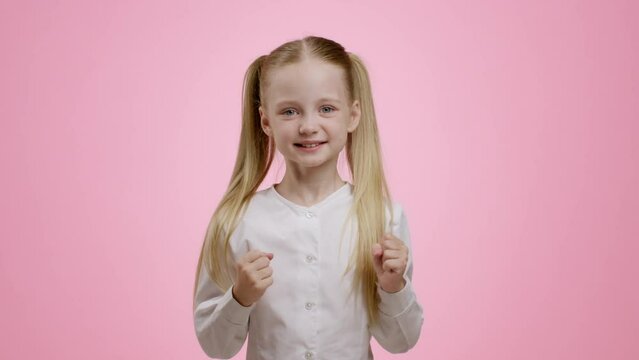 Cute happy little girl with ponytails enjoying success or present, laughing and gesturing, pink background, free space