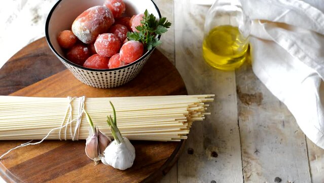 Ingredients of the italian "puttanesca" pasta: olives, pasta, capers, tomatoes, garlic and salad oil. Wooden background