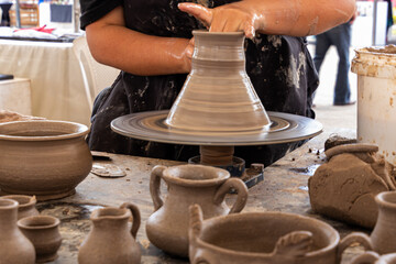 A potter man working on a potter's wheel making a ceramic pot out of clay. Master class on modeling on a potter's wheel. A few pots and jars not finished yet are in front of wheel