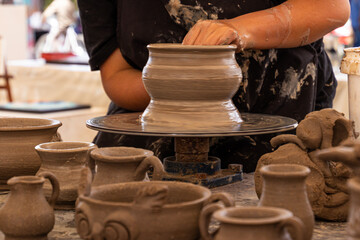 A potter man working on a potter's wheel making a ceramic pot out of clay. Master class on modeling on a potter's wheel. A few pots and jars not finished yet are in front of wheel
