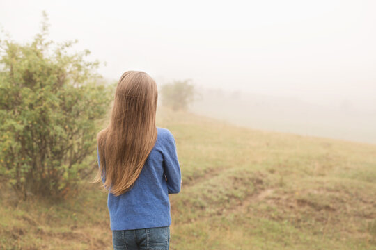 Long-haired girl walking on a foggy morning, back view